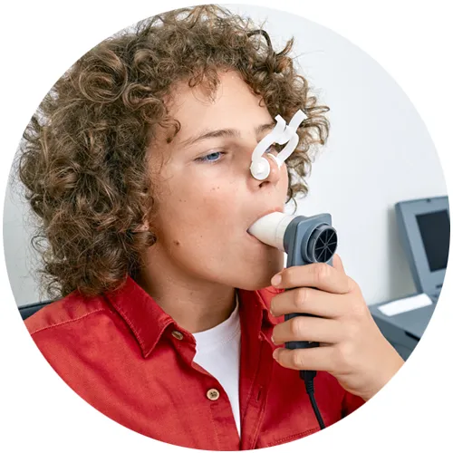 Boy with a nose clip blowing into a handheld spirometer during a breathing test